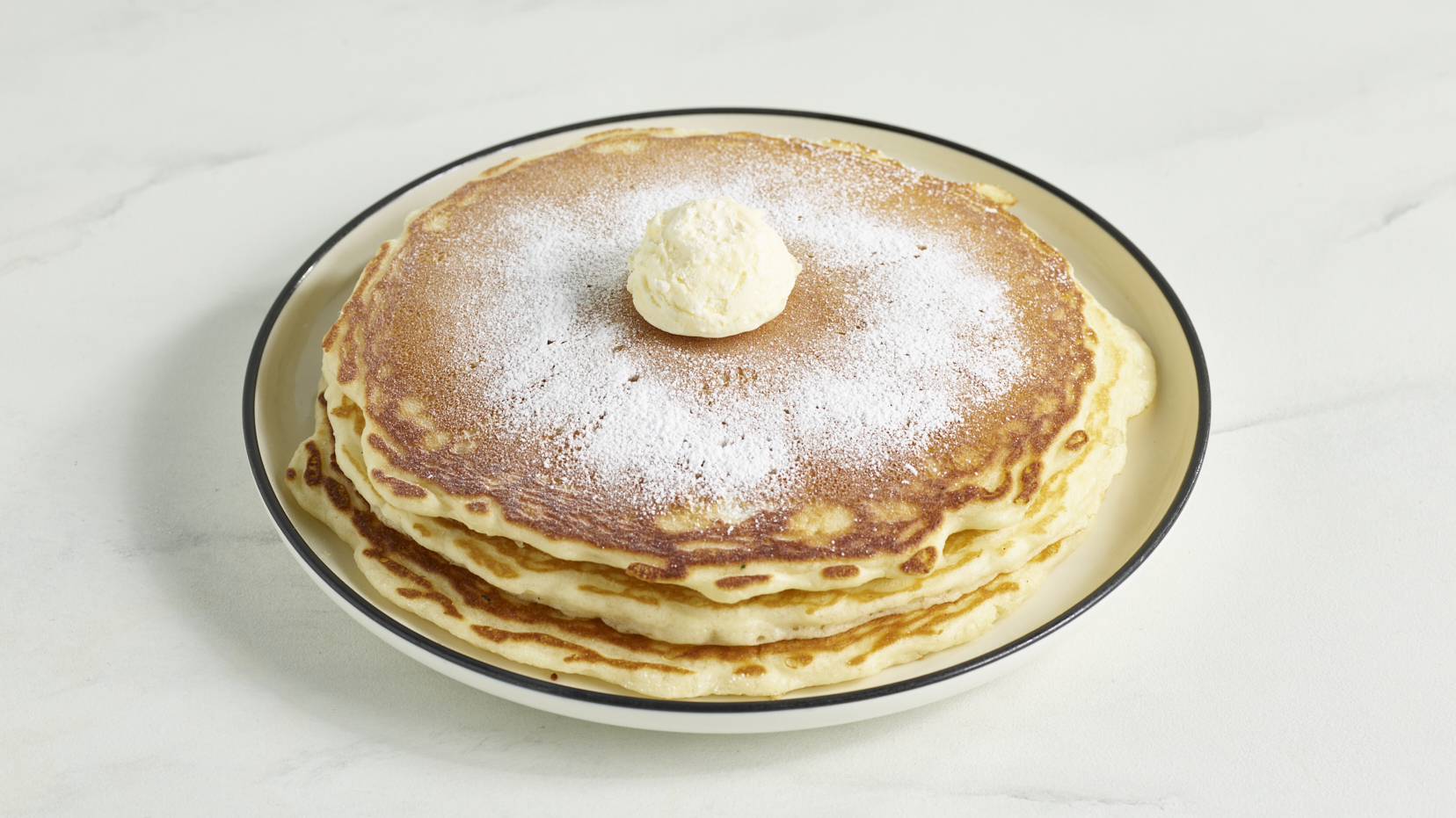 Fluffy stack of buttermilk pancakes with a pat of butter and powdered sugar