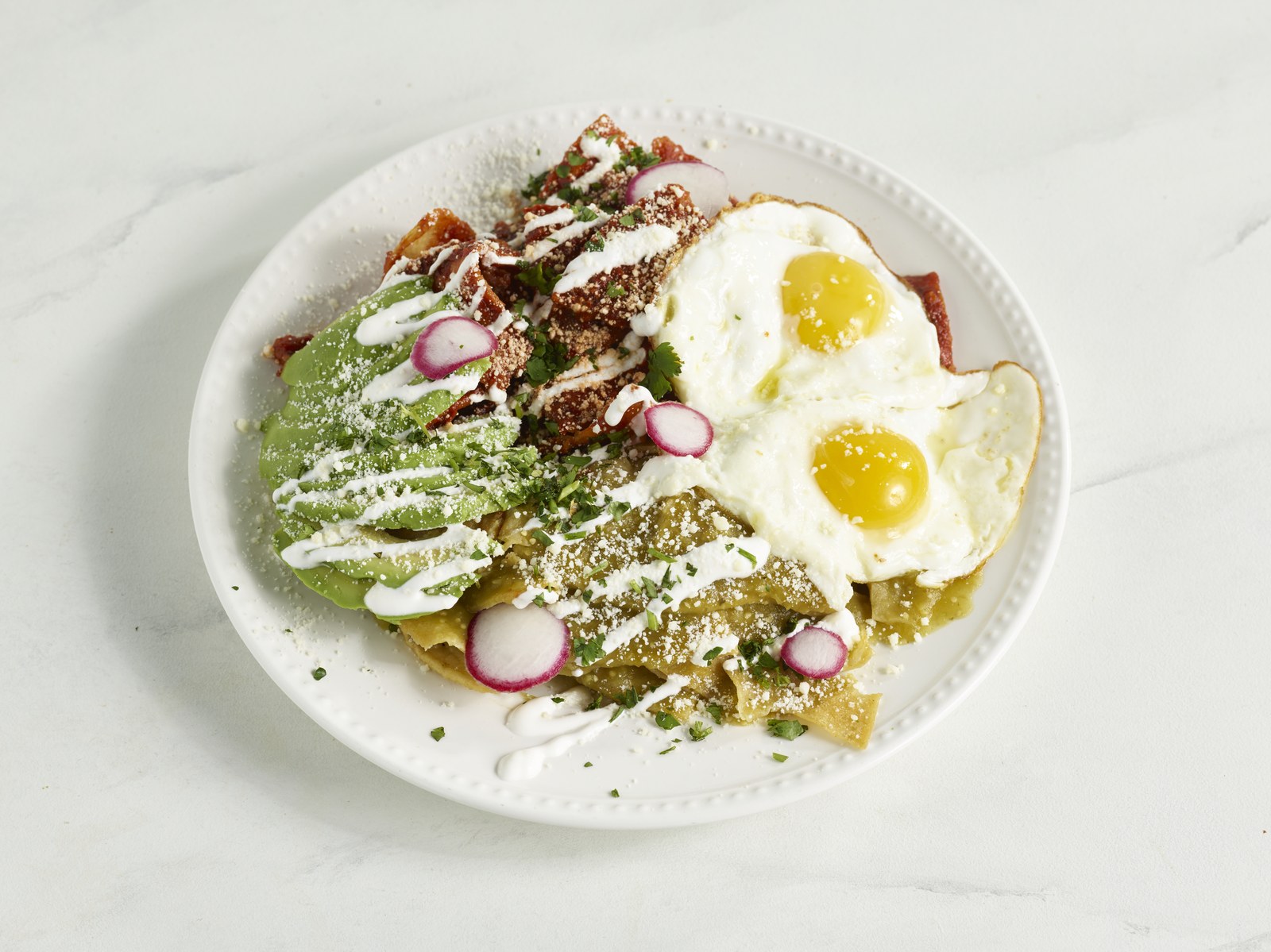 Chilaquiles Divorciados with red and green salsa, two eggs, crema and cotija cheese at Brunch & Beyond